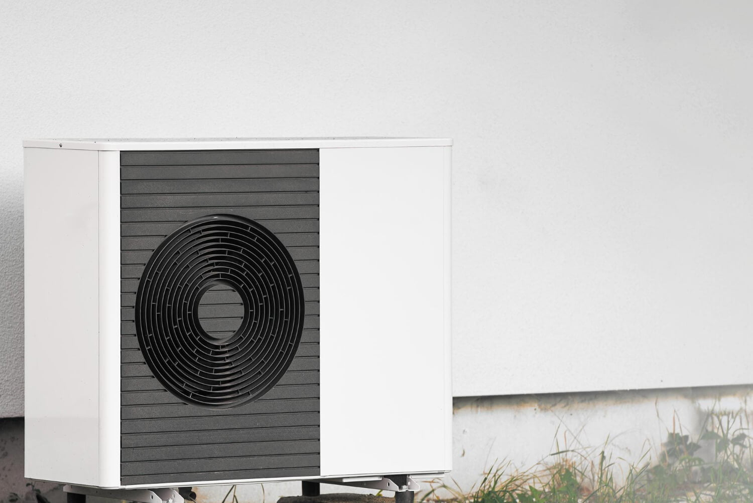 Buitenunit van een warmtepomp tegen een lichte gevel