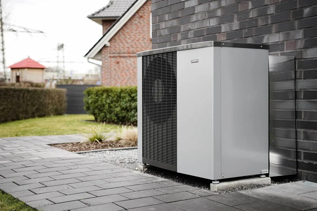 Buitenunit van een warmtepomp naast een woning met terras