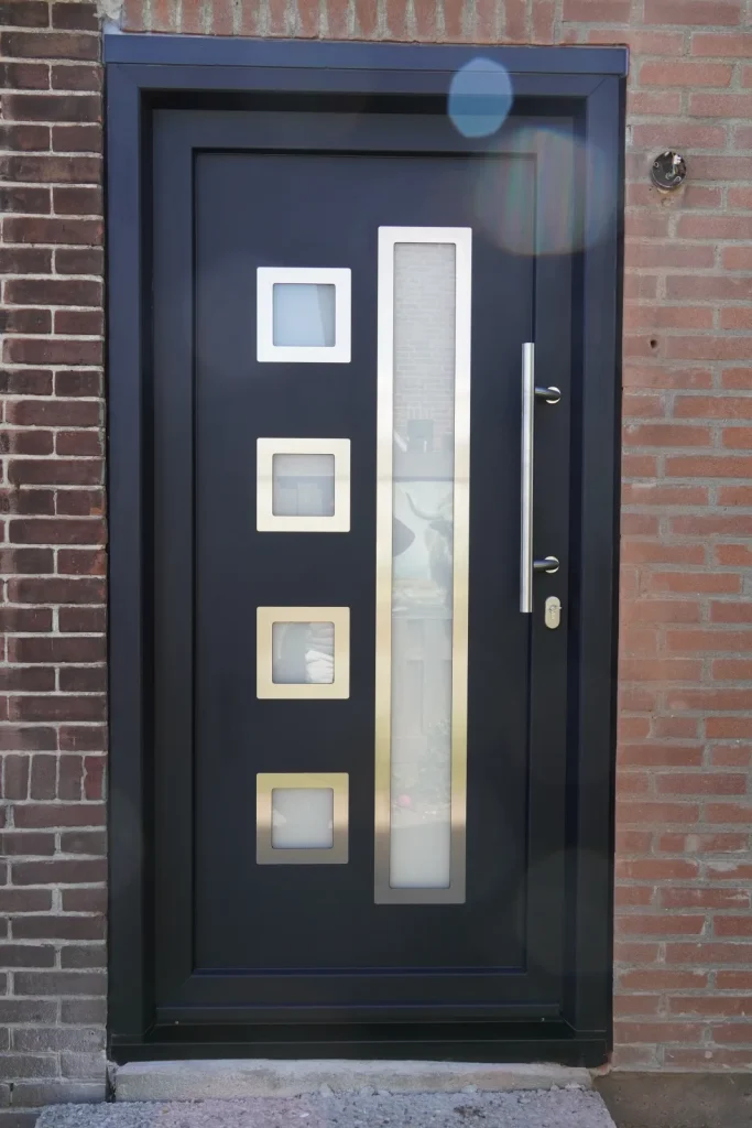 Antraciet voordeur met vier glasvakjes en een rvs-greep in een bakstenen gevel