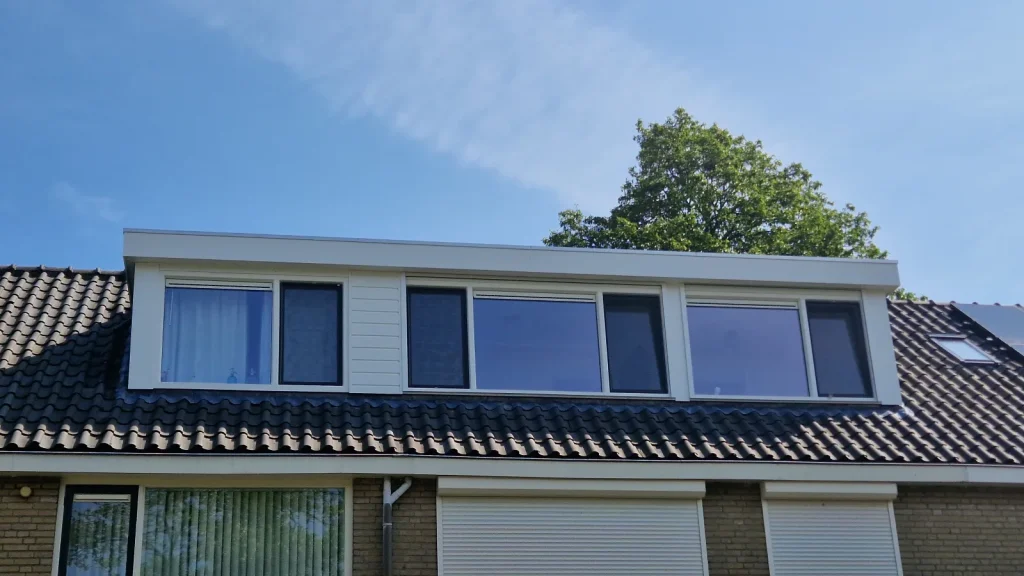 Brede witte dakkapel met kunststof kozijnen op een pannendak