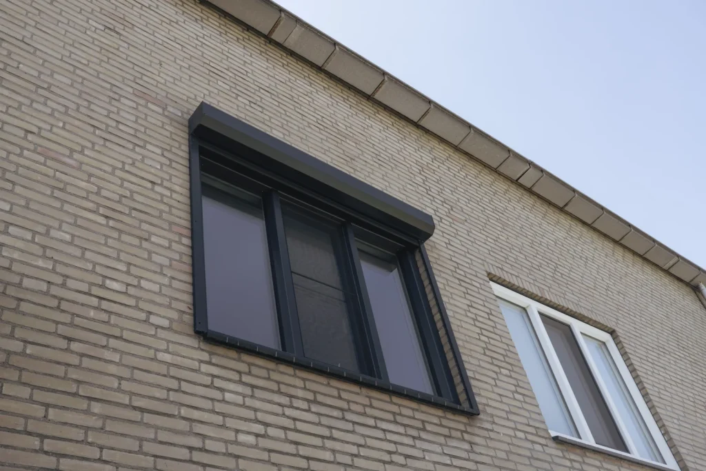 Donker kozijn met rolluik in een lichte bakstenen gevel