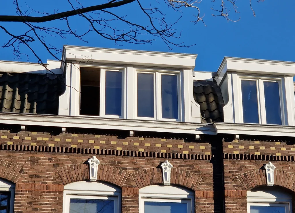 Twee klassieke witte dakkapellen met kroonlijst op een bakstenen herenhuis