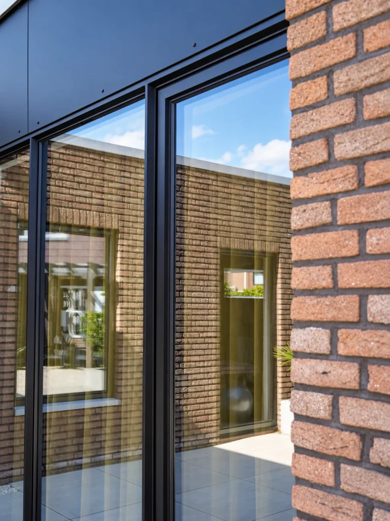 Slank antraciet kozijn met groot glasvlak naast bakstenen muur in Leiderdorp
