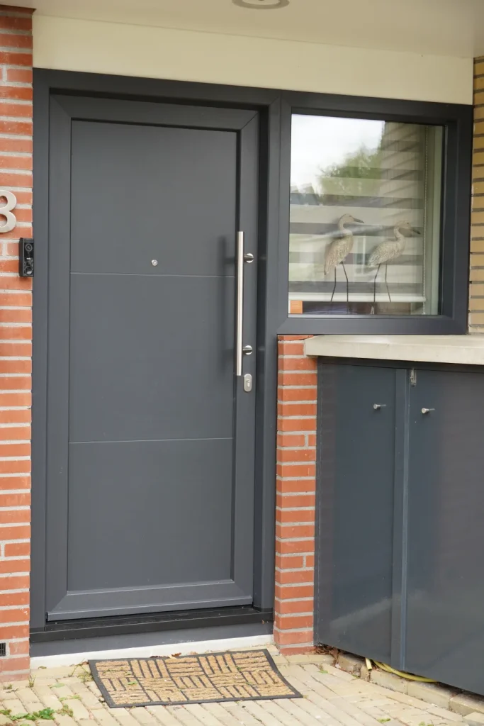 Strakke antraciet voordeur met lange greep en een raam ernaast