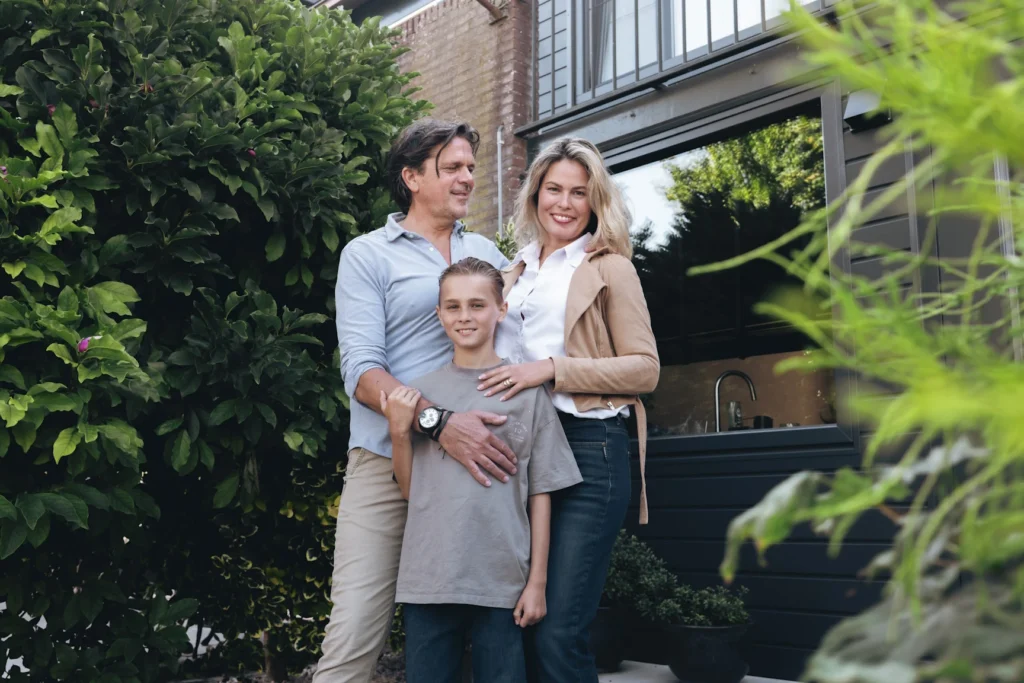 Gezin met zoon in de tuin voor hun woning met donkere kozijnen